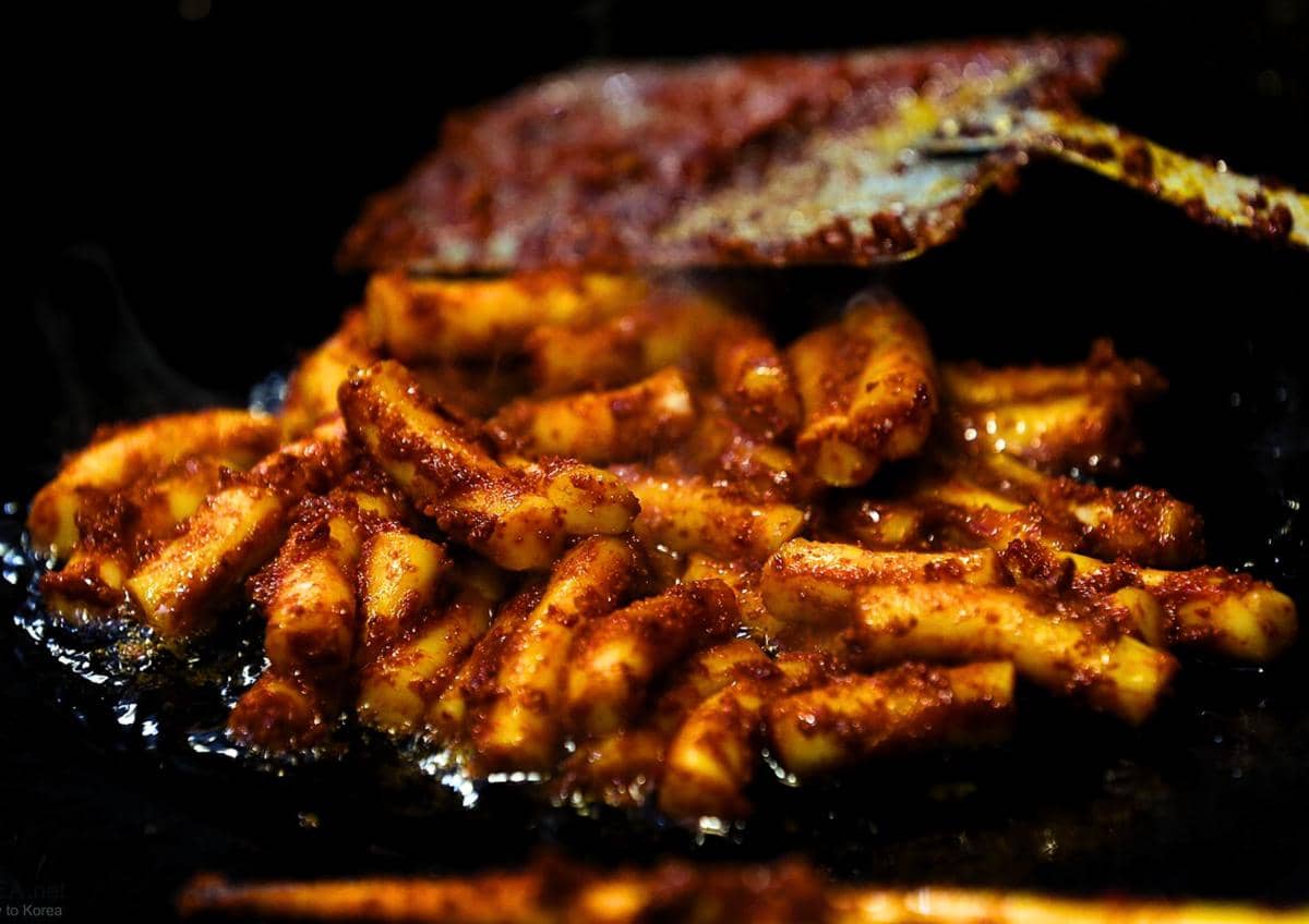 Ilustrasi gireum tteokbokki khas Korea Selatan berupa kue beras silinder goreng dengan bumbu pedas gurih.