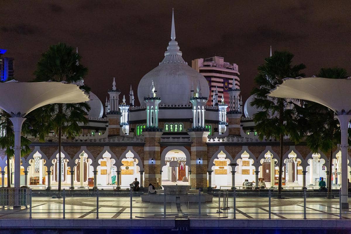 Masjid Jamek tampak bercahaya pada malam hari, dengan kubah dan menara yang menonjol di bawah langit gelap.