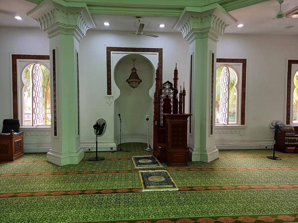 Interior aula salat Masjid Jamek dengan mihrab dan mimbar sebagai titik utama di bagian depan ruangan.