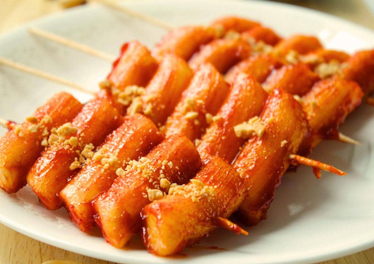 Ilustrasi tteok kochi, sate kue beras Korea berbentuk silinder yang ditusuk dan diberi saus merah pedas.