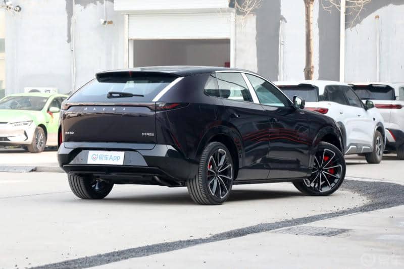 Tampilan buritan Mazda CX-6e berwarna gelap dengan lampu belakang tipis, logo Mazda, dan tulisan model pada pintu bagasi.