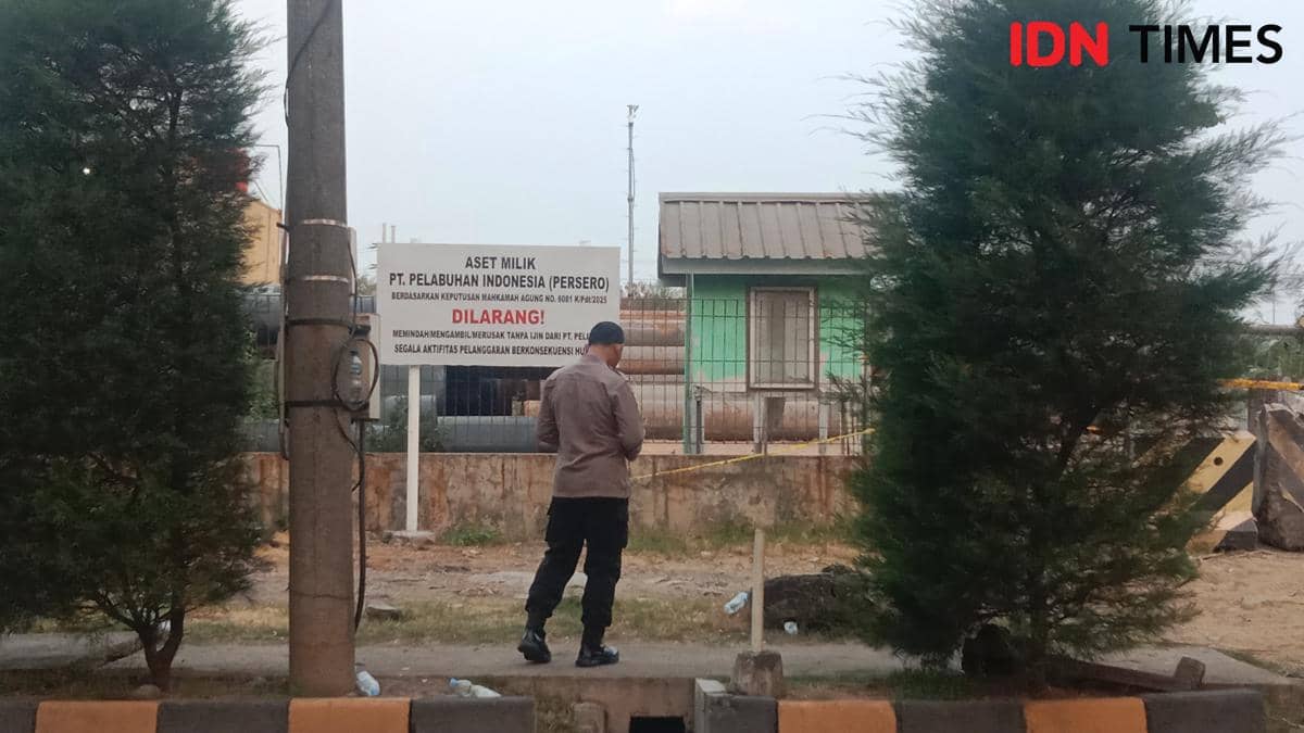 Seorang polisi berseragam berdiri di depan papan plang larangan yang dipasang Pelindo di area luar ruangan.