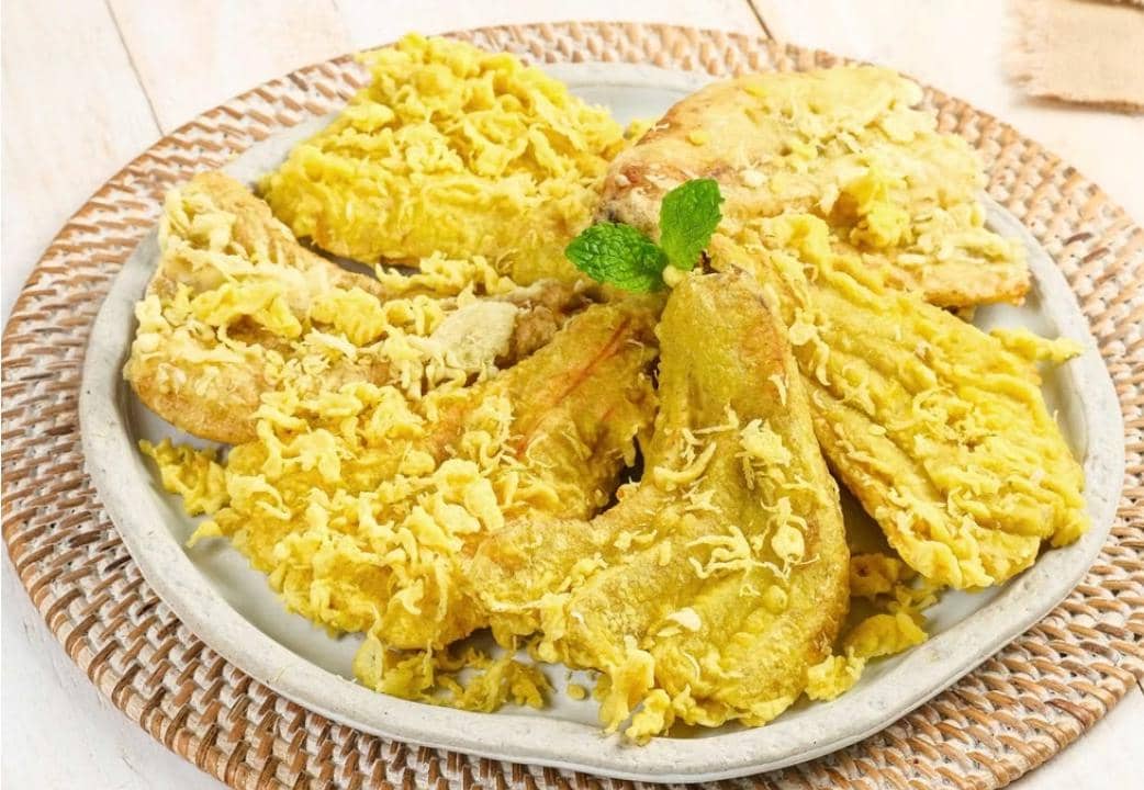 Sepiring pisang goreng berwarna keemasan tersaji sebagai ilustrasi camilan tradisional Indonesia yang hangat.