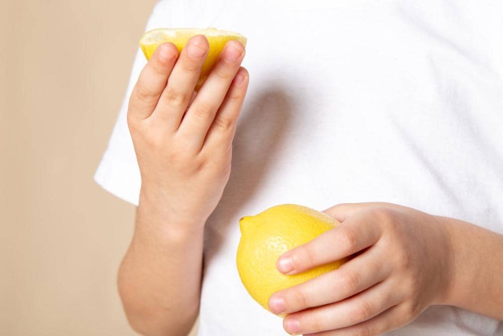 Ilustrasi perasan lemon kuning dengan cairan yang menetes dari potongan buah ke sebuah wadah di bawahnya.