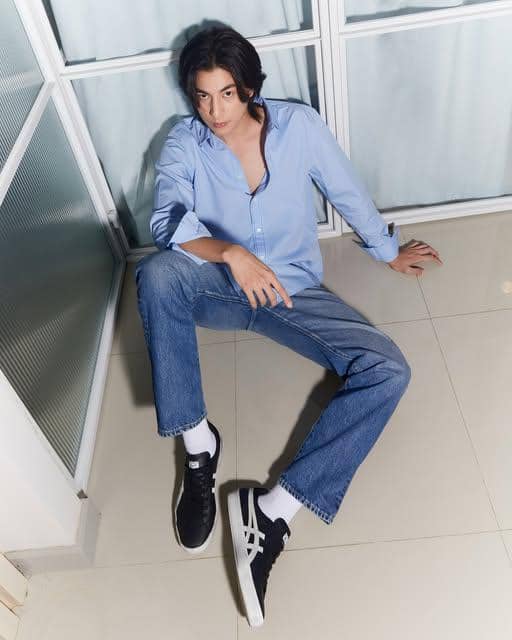 Gulf Kanawut mengenakan busana kasual bernuansa gelap dengan sneakers kanvas untuk gaya OOTD santai.
