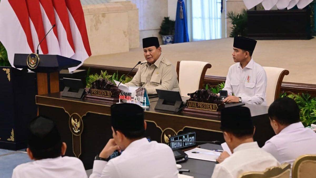 Suasana Sidang Kabinet Paripurna: dua pejabat berpeci hitam duduk di meja bertanda "Presiden RI" dan "Wakil Presiden RI", dengan para menteri berbaju putih duduk di depan mereka.