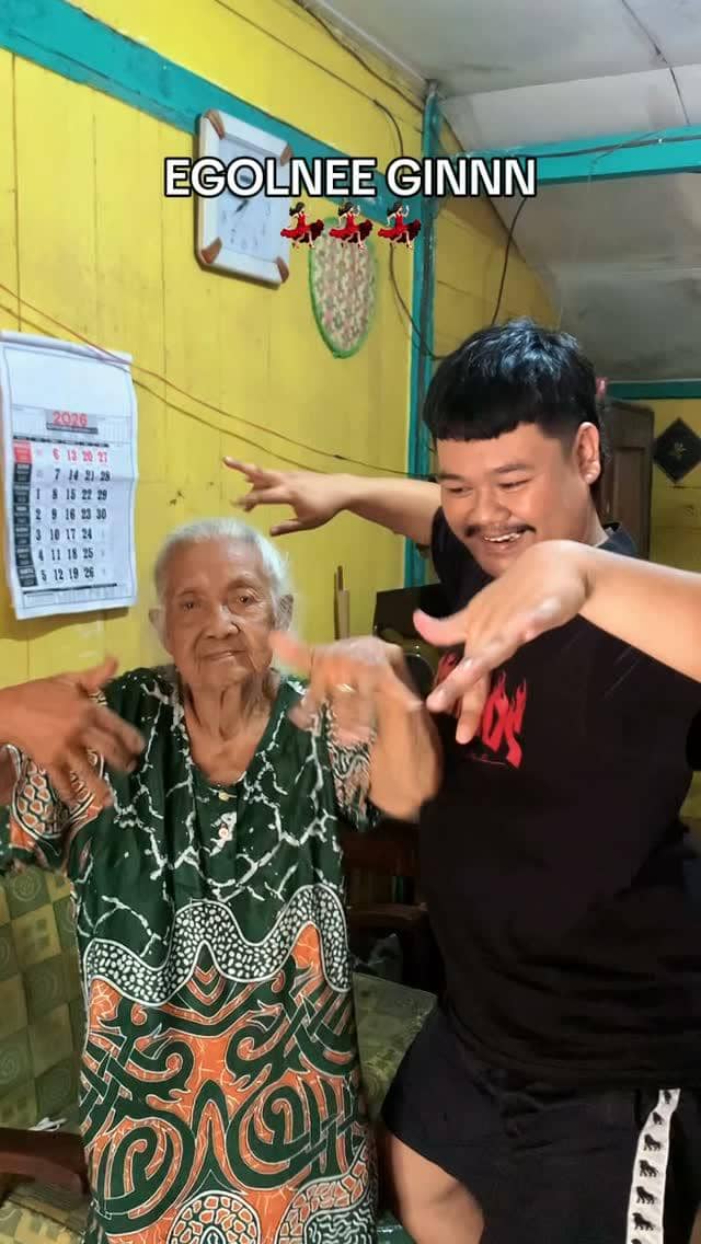 Refido dan Mbah Leginah berpose bersama di luar ruangan, mengenakan pakaian kasual sambil tersenyum ke kamera.