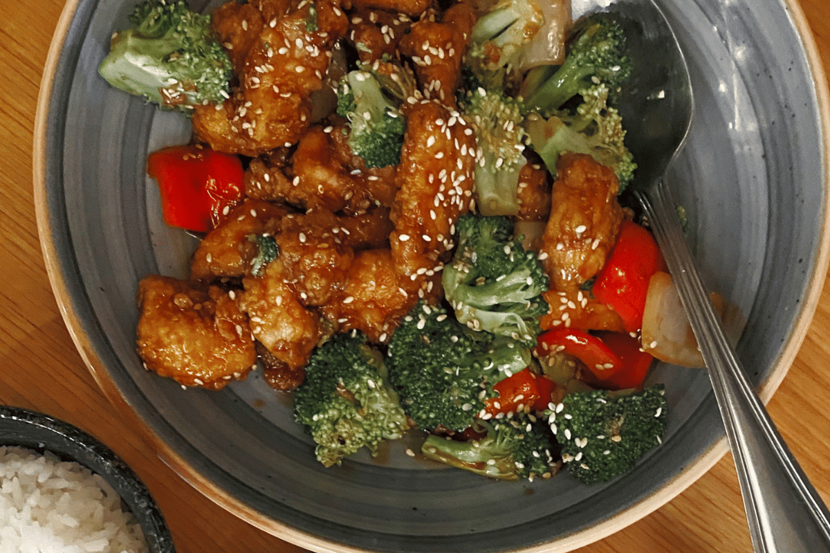 Seporsi chicken broccoli ala Chinese takeout dengan potongan ayam dan brokoli hijau dalam saus gurih di atas nasi.