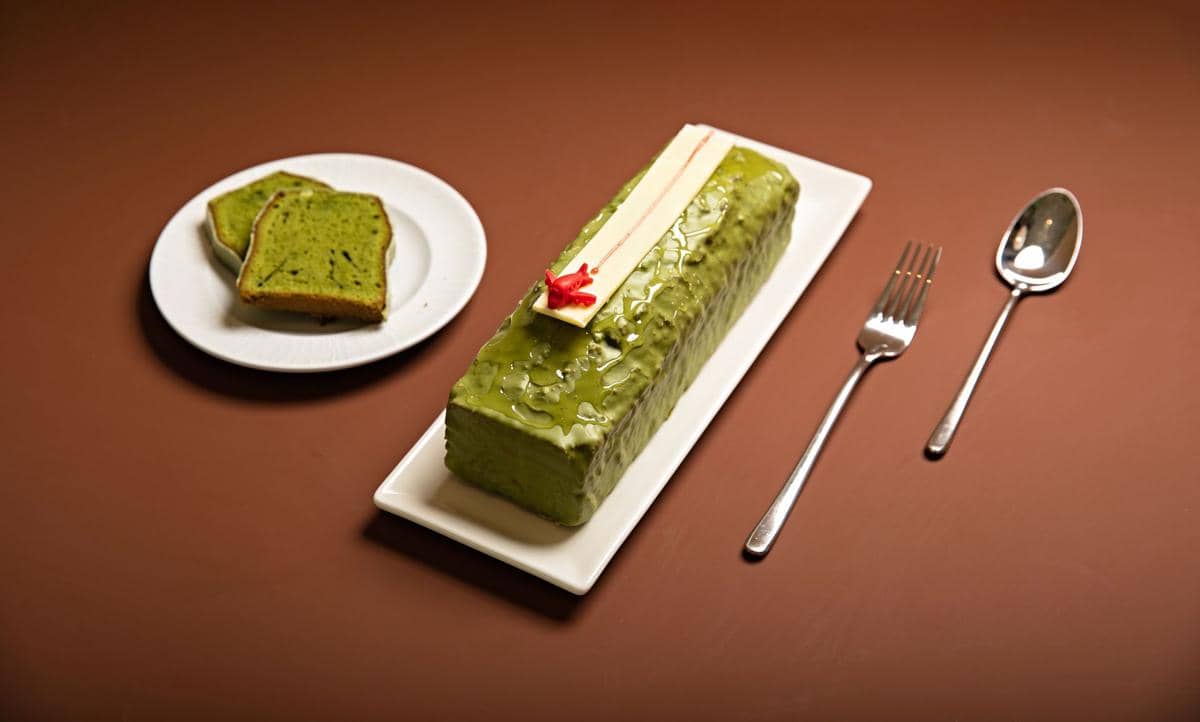 Segelas minuman ube matcha berlapis warna ungu dan hijau, disajikan dingin sebagai ilustrasi kuliner.