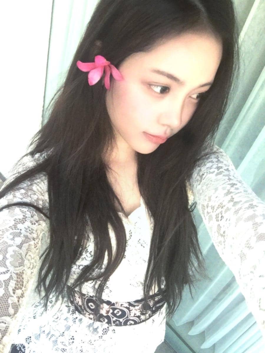 Carmen dari Hearts2Hearts mengenakan kebaya Bali putih dengan hiasan bunga di rambut saat berpose.