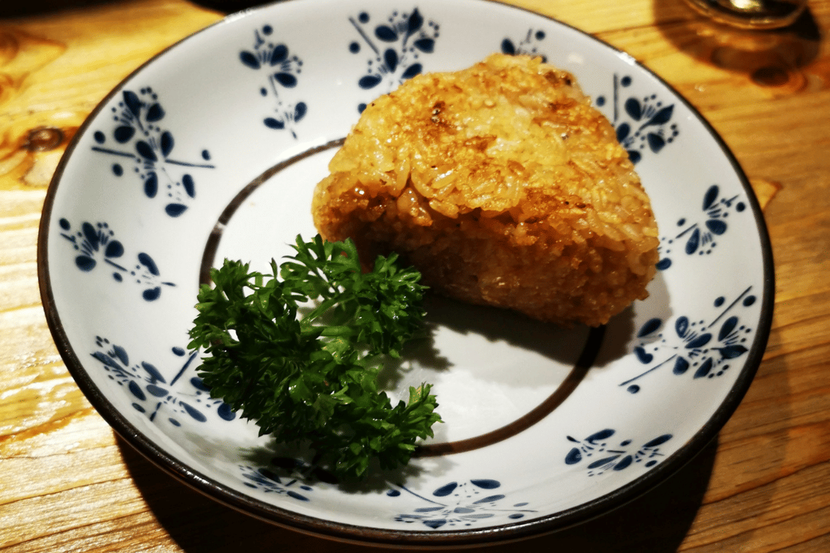 Ilustrasi tamago onigiri berupa nasi kepal Jepang segitiga dengan telur dan lembaran nori di bagian tengah.