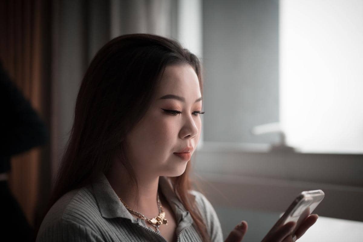 Seorang perempuan sedang menatap dan membaca informasi di layar ponsel pintar dengan tatapan fokus