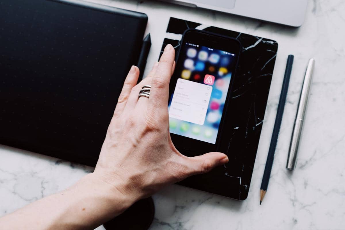 Seseorang menggunakan smartphone ketika sedang mengerjakan aktivitas lain di meja