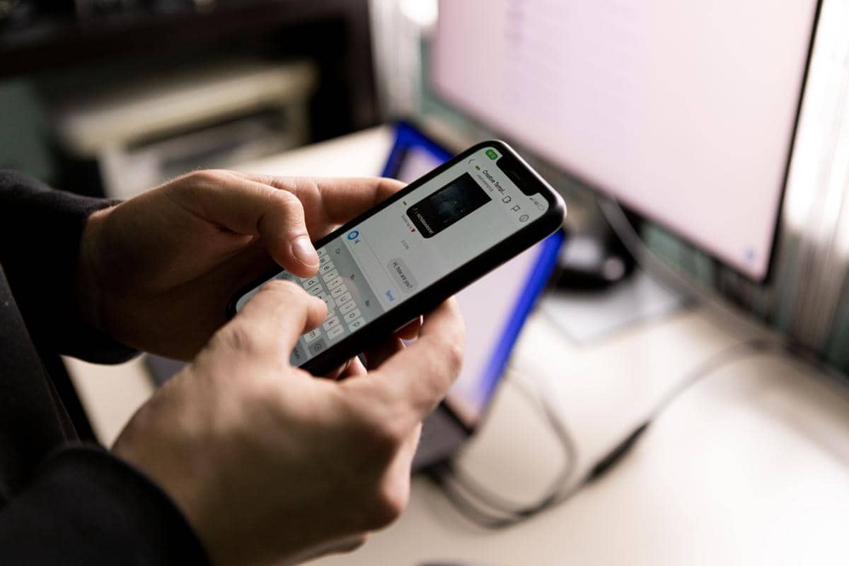 Seseorang sedang menggunakan smartphone sambil berada di depan komputer