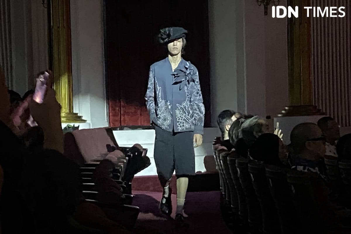 Seorang perempuan mengenakan look biru-abu berupa jaket bermotif floral dalam potret fesyen bergaya kasual.