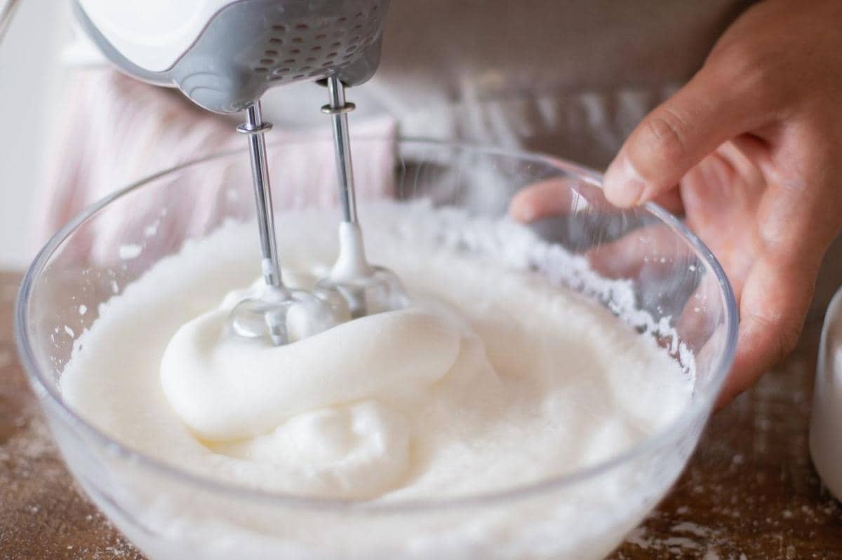 Tangan menggunakan mixer listrik untuk mengocok krim dalam mangkuk agar whipped cream mengembang kokoh.