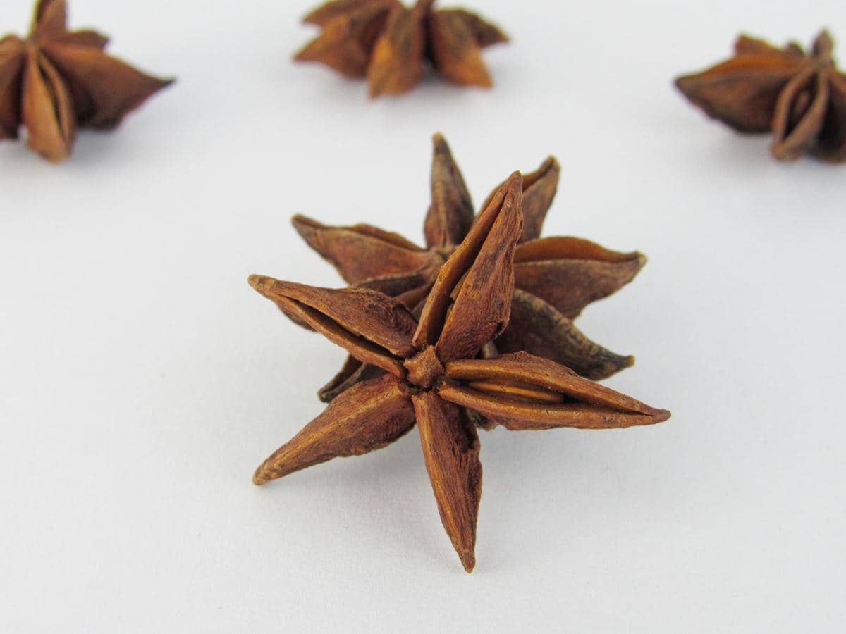 Ilustrasi bunga lawang atau anise berbentuk bintang berwarna cokelat di atas permukaan kayu dengan latar gelap.