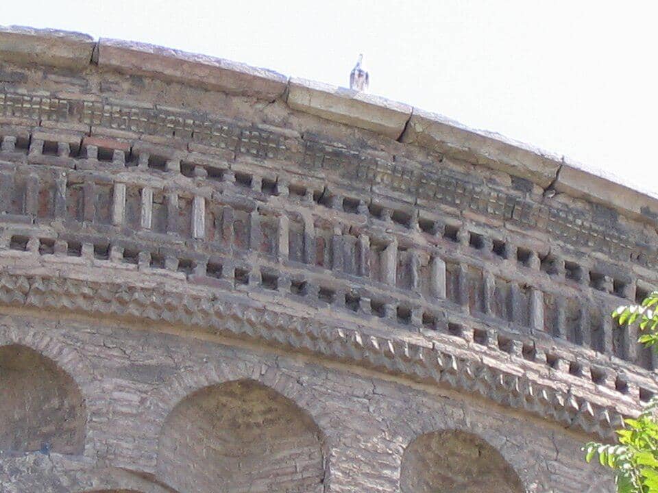Detail ornamen bata geometris pada kornis Menara Toghrol, memperlihatkan susunan bata merah kecokelatan yang rumit.
