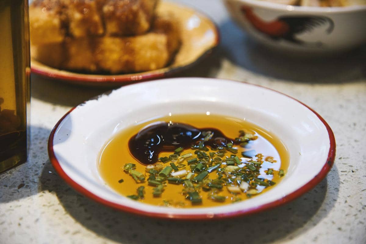 Semangkuk saus cokelat dengan irisan daun bawang dan wijen sebagai pelengkap hidangan udon hangat.