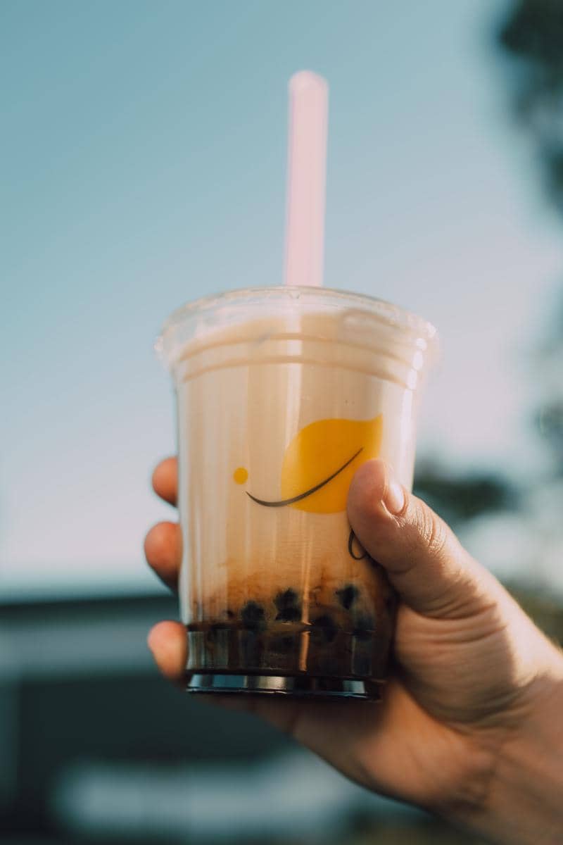 Tangan memegang gelas plastik minuman boba milk tea dengan sedotan