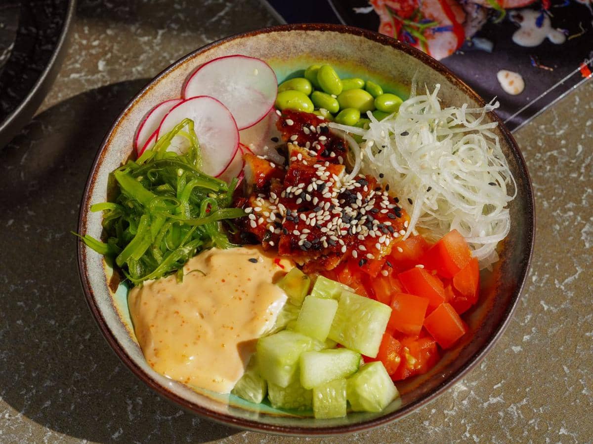 Semangkuk poke bowl berisi nasi, salmon, alpukat, edamame, dan sayuran segar sebagai ilustrasi hidangan sehat.