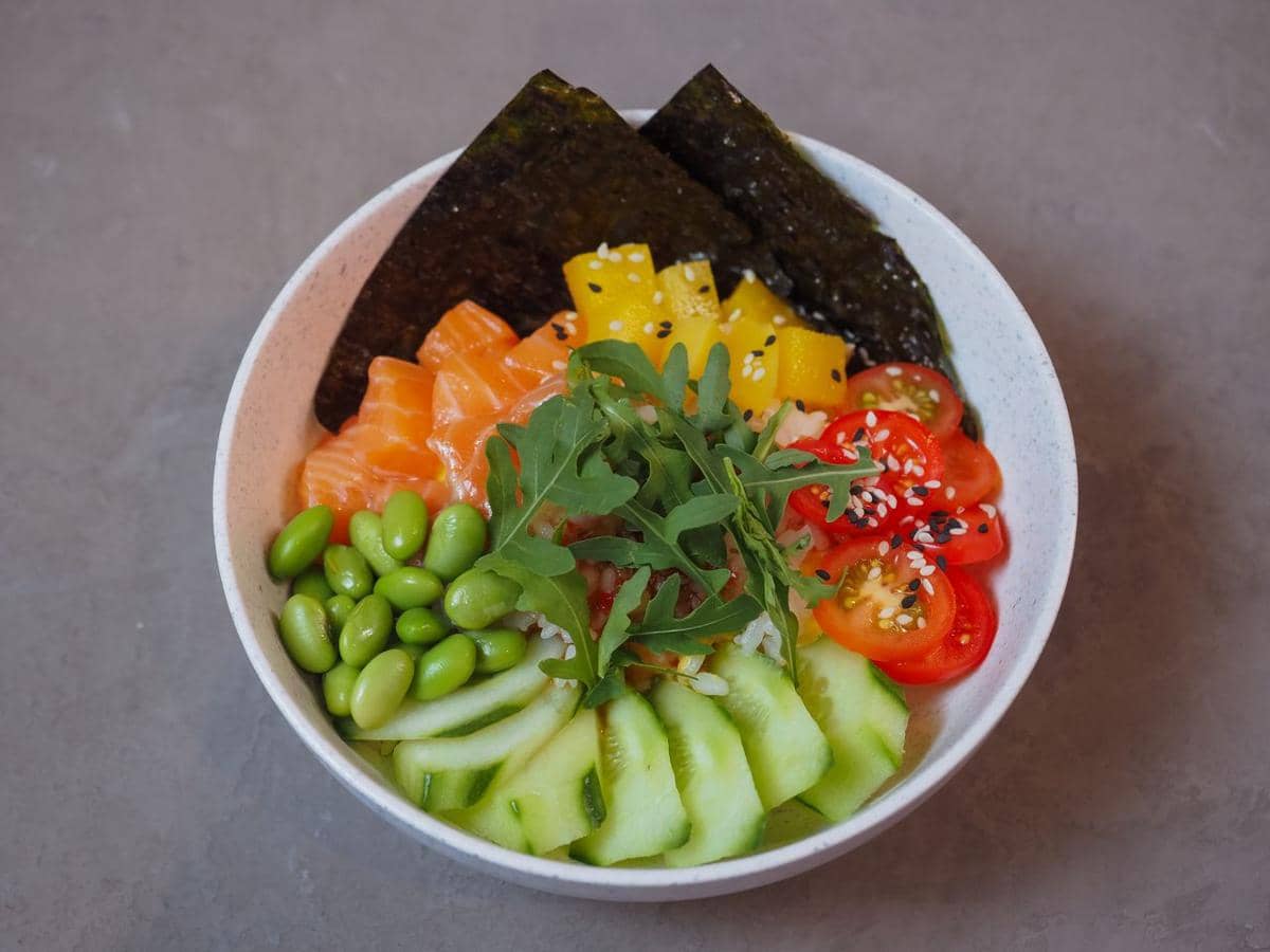 Ilustrasi semangkuk poke dengan susunan nasi dan aneka topping, menggambarkan sajian sehat yang berwarna-warni.