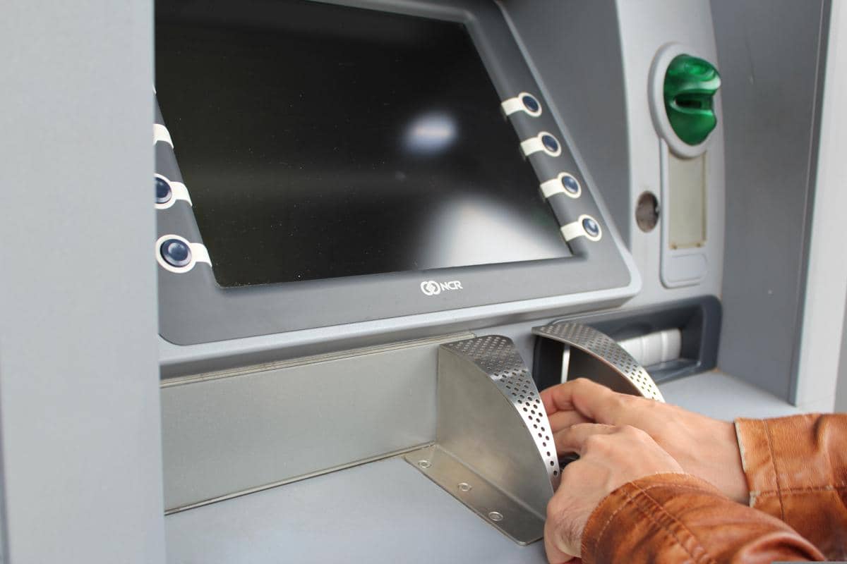 Tangan seseorang mengambil uang dari slot mesin ATM