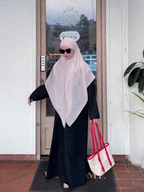 Adinda Amira tampil dengan abaya hitam longgar, jilbab senada, tas tangan, dan kacamata hitam saat berpose.