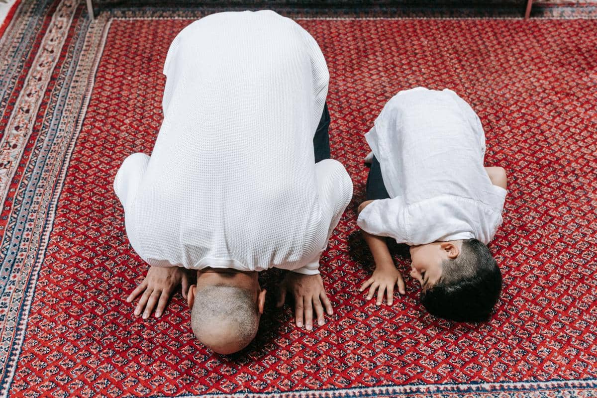 Ilustrasi orang dewasa mengajarkan seorang anak salat sebagai bagian dari pendidikan agama di rumah bersama keluarga.