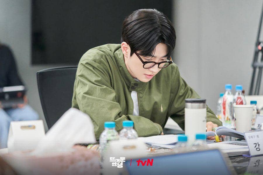 Happy Anding sedang membaca naskah dengan fokus dalam dokumentasi tvN pada kegiatan pembacaan naskah.