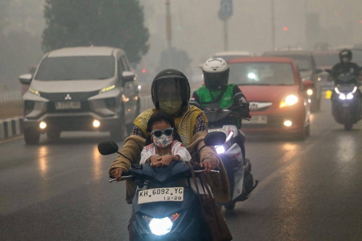 Seorang ibu dan anaknya yang mengenakan masker berkendara sepeda motor menembus kabut asap pekat akibat kebakaran hutan dan lahan di wilayah