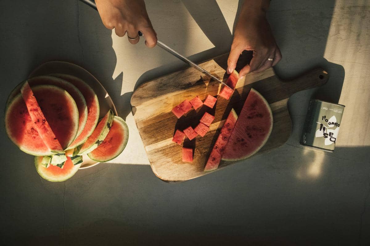 Potongan semangka merah dan kulitnya tersaji di atas talenan kayu sebagai ilustrasi bahan asinan kulit semangka.