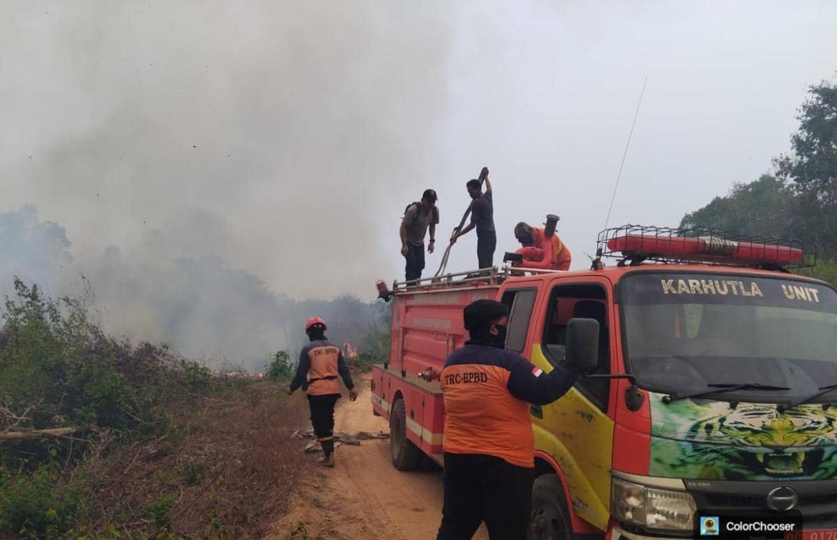 Petugas BPBD Muba menyemprotkan air untuk memadamkan api di lahan terbakar dengan latar vegetasi dan asap.