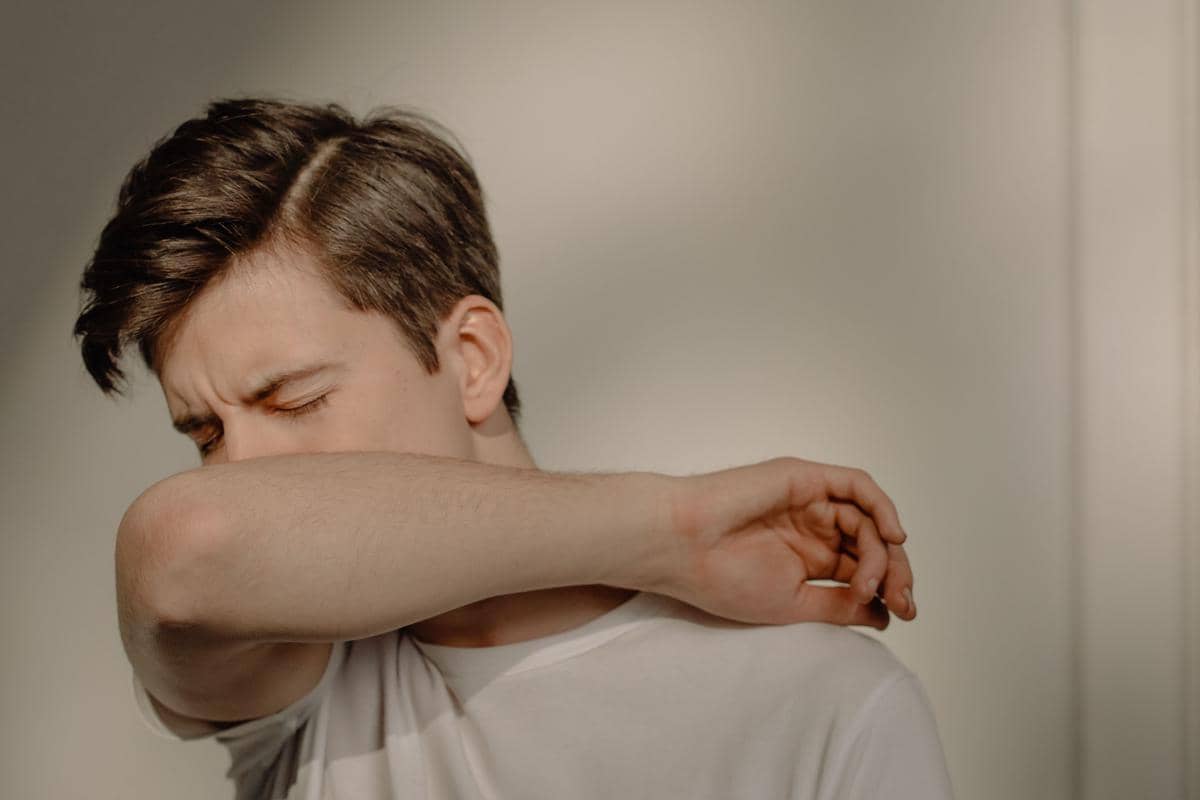Seorang pria berpakaian kaus putih menutupi hidung dan wajahnya dengan lipatan lengan untuk mengecek aroma ketiaknya.
