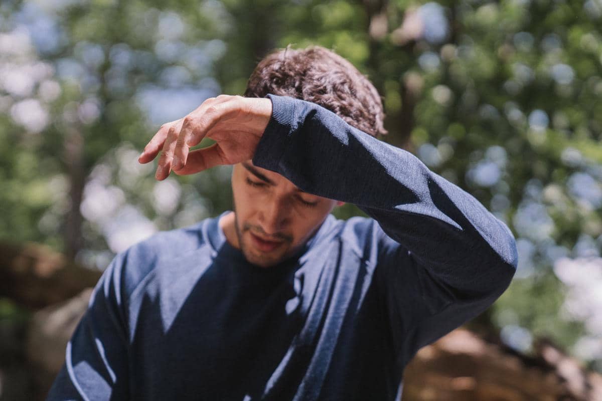 Seorang pria mengenakan baju lengan panjang biru mengusap dahi dengan tangannya karena kepanasan di bawah sinar matahari.
