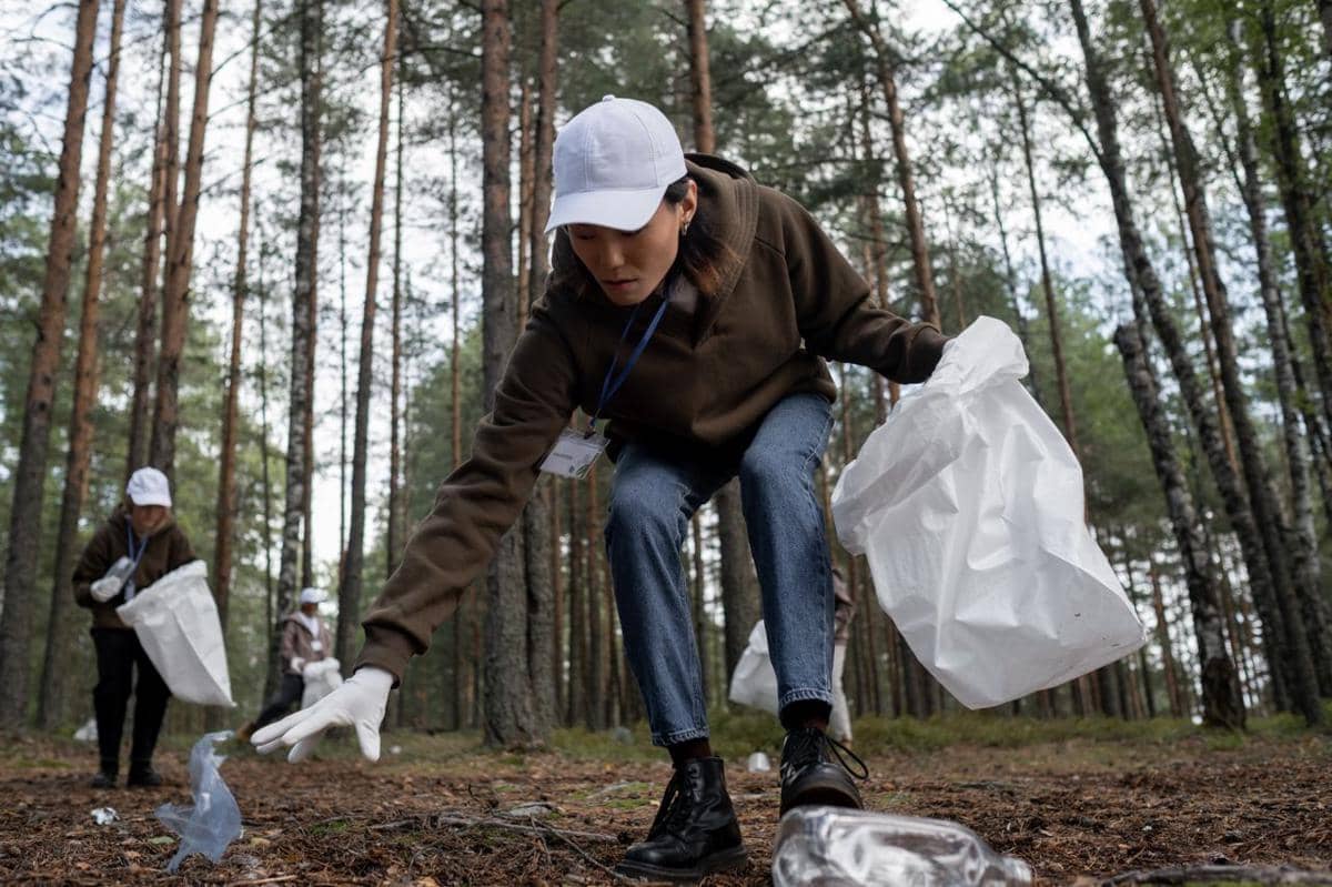Ilustrasi seseorang mengenakan sarung tangan sambil memungut sampah dan memasukkannya ke dalam kantong plastik.