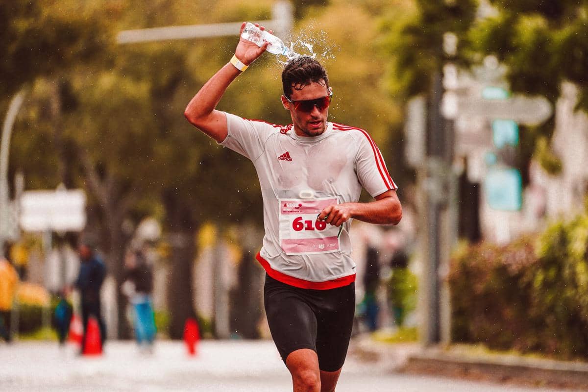 Seorang pria pelari maraton bernomor dada mengguyur kepalanya dengan botol air mineral saat berlari di jalan raya.