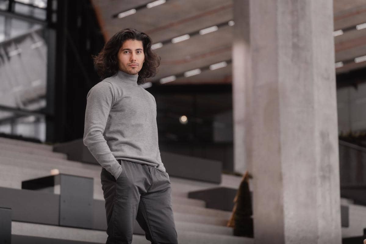 Pria berambut panjang mengenakan baju turtleneck abu-abu dan celana panjang warna abu-abu tua