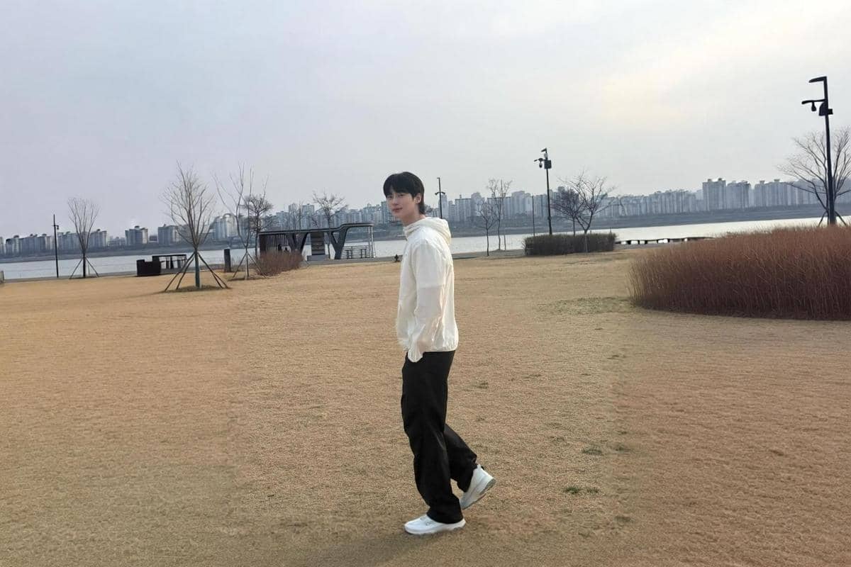 Byeon Woo Seok berdiri di area terbuka memakai jaket windbreaker putih dan celana kargo hitam serta sneakers putih