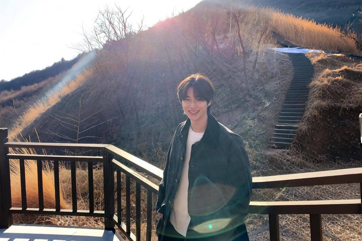 Byeon Woo Seok tersenyum memakai kemeja luar hijau olive tebal dengan kaus rajut putih di dalamnya