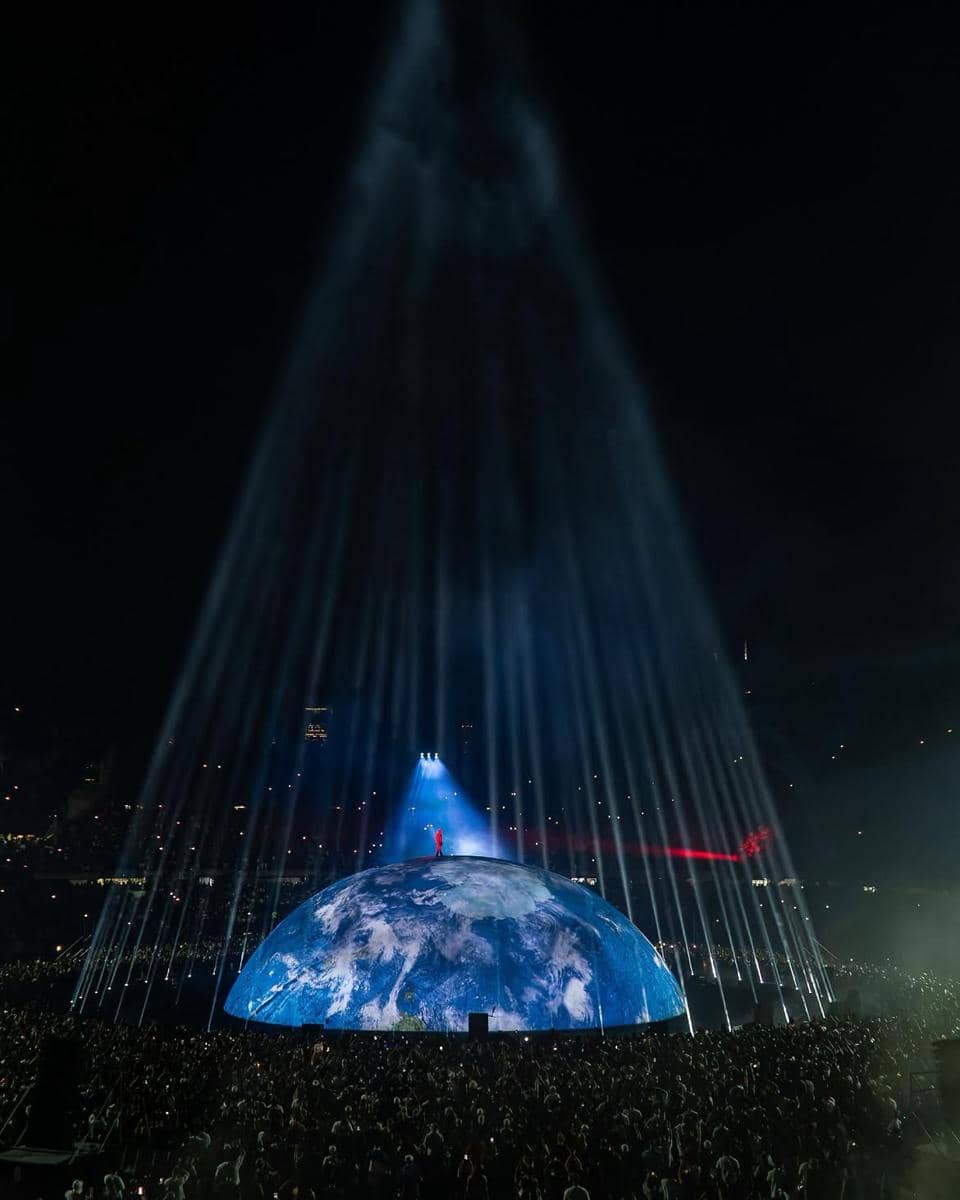 Ye tampil di atas panggung saat konser di Jakarta, dikelilingi cahaya merah dan layar visual di belakangnya.