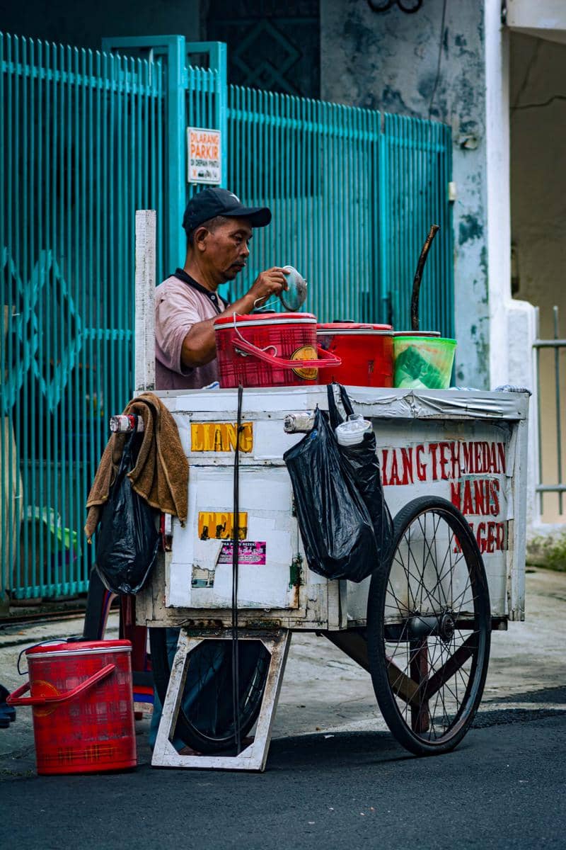 Seorang pedagang menyiapkan minuman tradisional di gerobak putih di pinggir jalan.