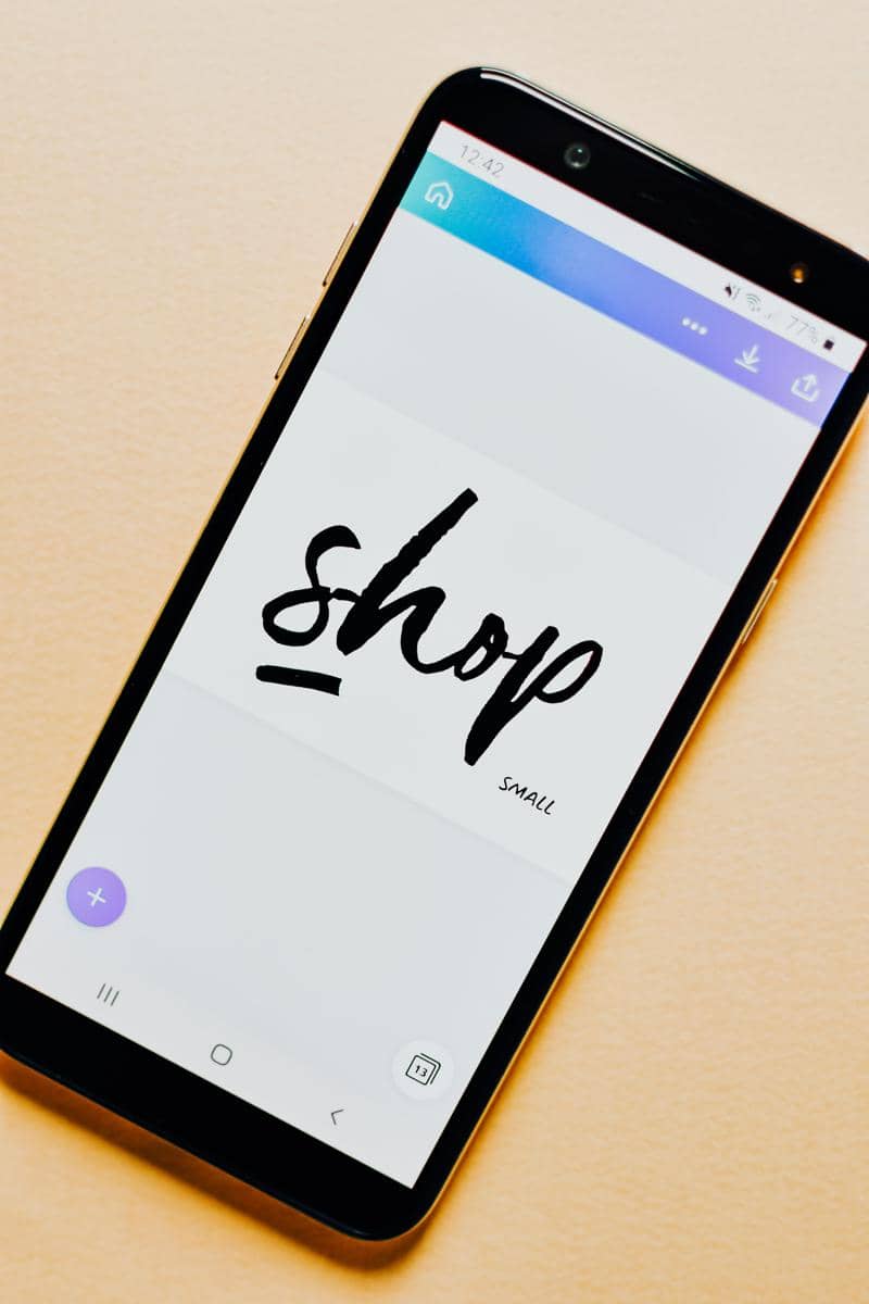 Smartphone menampilkan tulisan Shop pada layar sebagai ilustrasi bisnis digital.