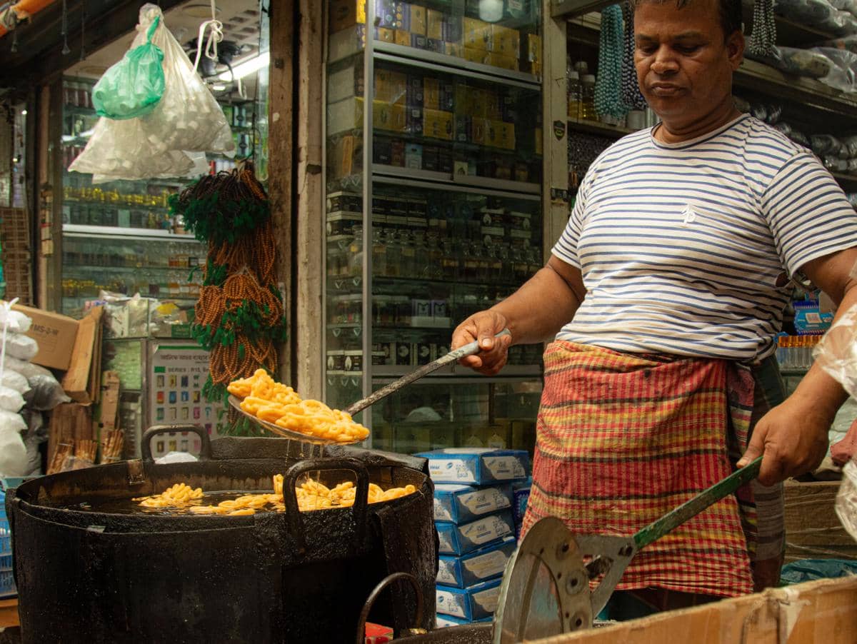 Pedagang menggunakan alat penggorengan besar untuk memasak camilan di kios makanan.