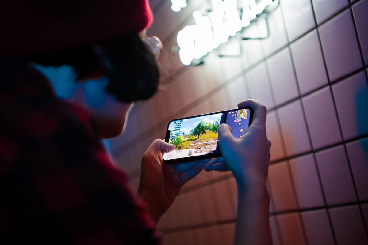 Seseorang bermain game di smartphone dengan kedua tangan, menampilkan aktivitas gaming mobile di layar.