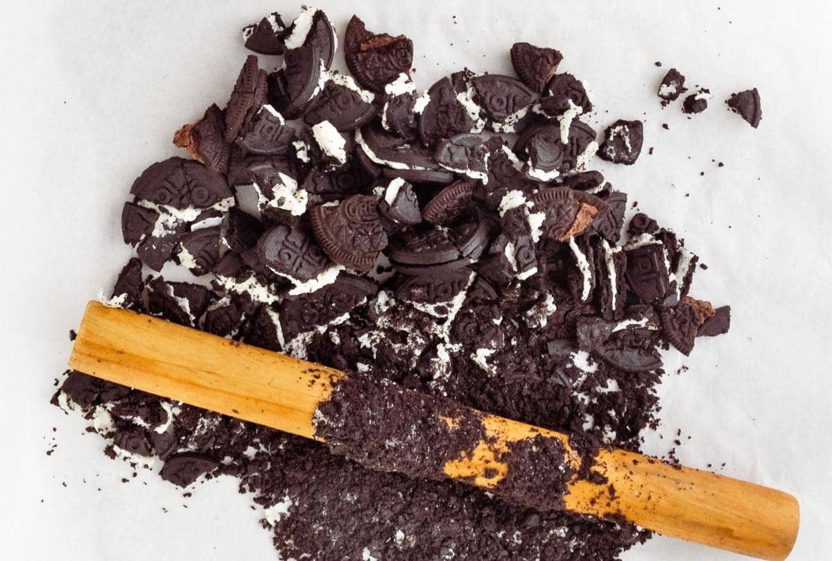 Ilustrasi biskuit Oreo berwarna gelap yang dihancurkan hingga menjadi remah-remah di atas permukaan putih.