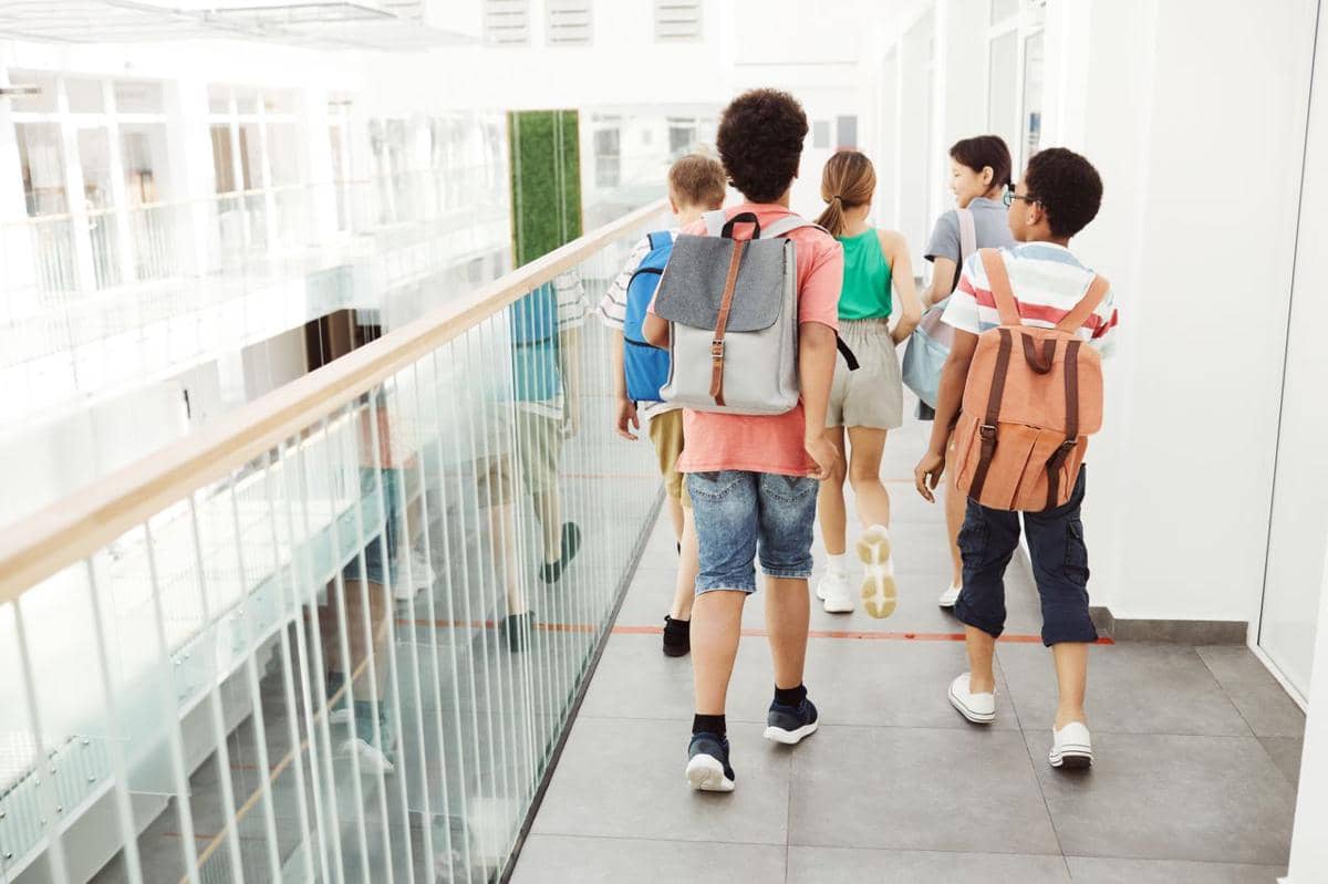 Ilustrasi sekelompok anak-anak berjalan di dalam lorong sekolah sambil membawa ransel.