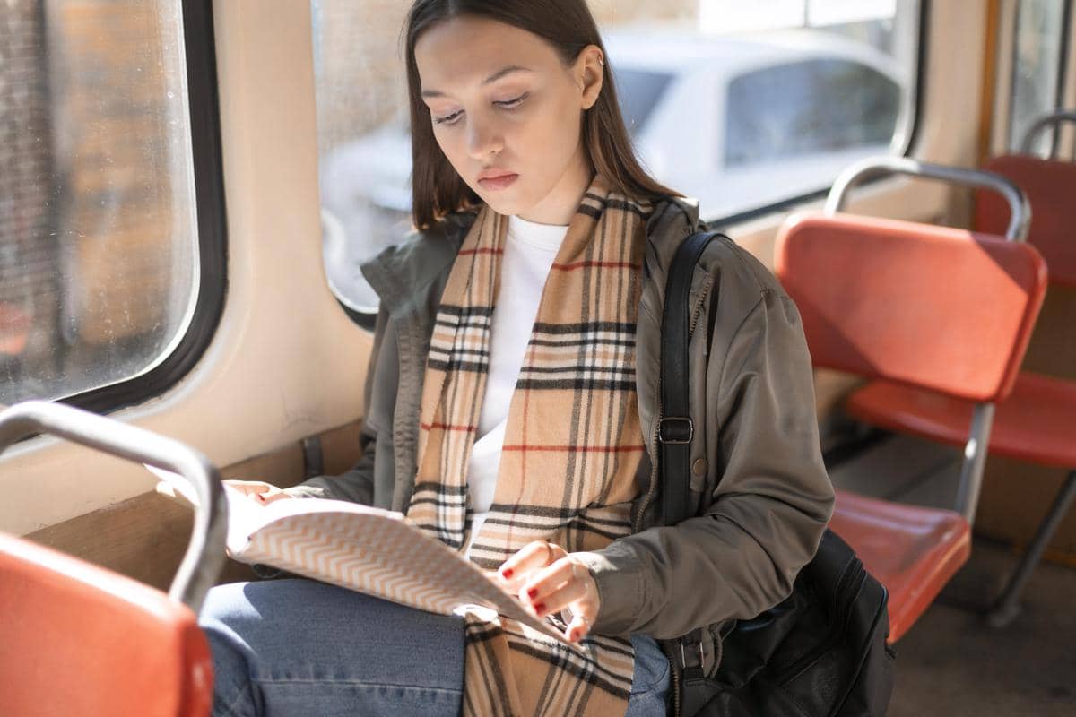Seorang penumpang membaca buku sambil duduk di dalam bus dalam ilustrasi perjalanan dengan transportasi umum.