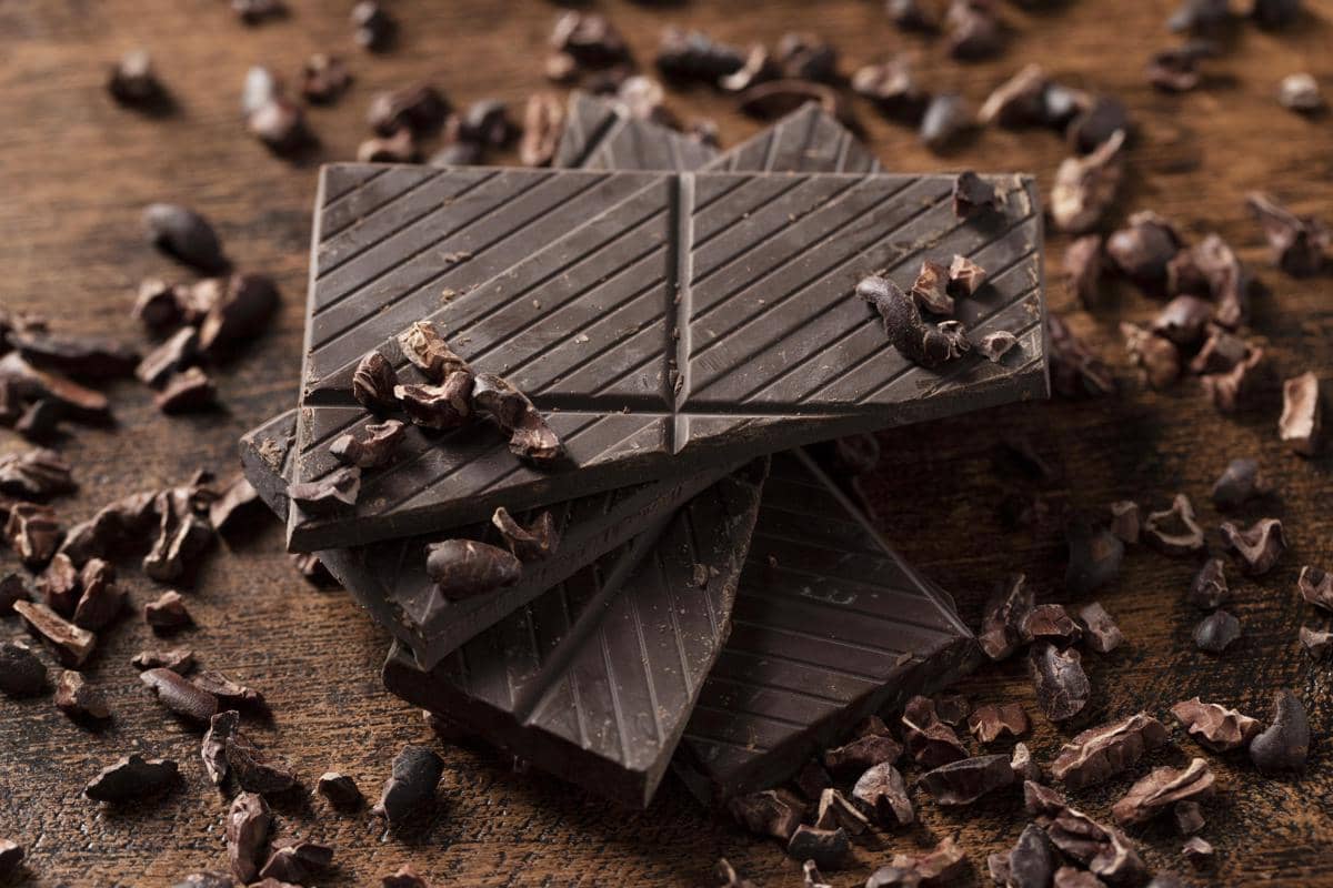 Ilustrasi cokelat hitam dengan potongan batangan cokelat berwarna cokelat gelap sebagai gambaran produk cokelat.
