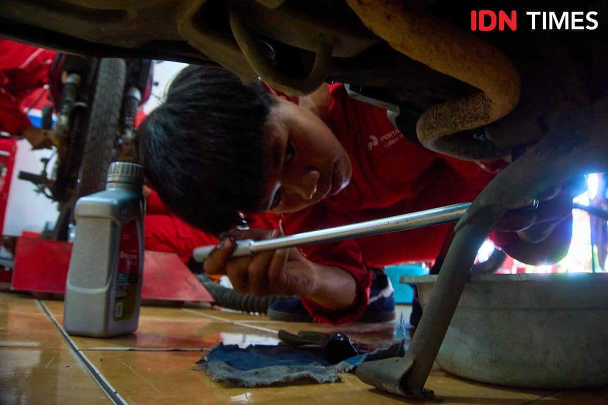 Seorang siswa Jurusan Teknik Sepeda Motor (TSM) SMK Harapan Mulya memeriksa bagian bawah mesin sepeda motor pelanggan di bengkel teaching fa